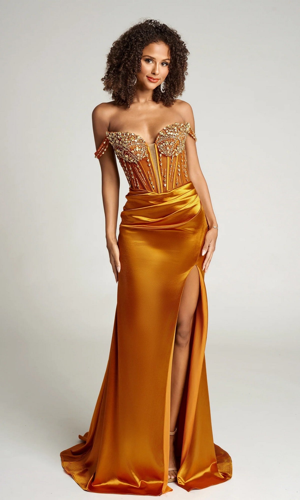 Woman wearing the bronze Portia and Scarlett PS26046 long formal dress, featuring an off-the-shoulder beaded corset bodice and high leg slit, standing against a plain background.